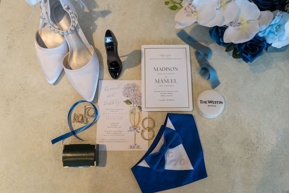 Wedding invitations and blue decor items scattered on a textured beige surface create an elegant flat lay composition.