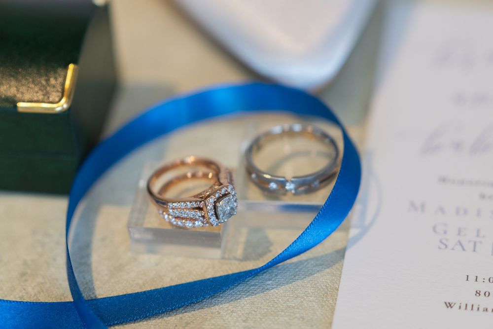 Close-up view of a diamond engagement ring displayed on a white surface with a blue ribbon accent creating elegant shadows.