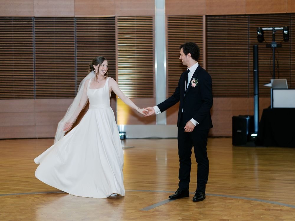 A couple performs their first dance in an elegant reception hall with wooden walls and polished hardwood floors.