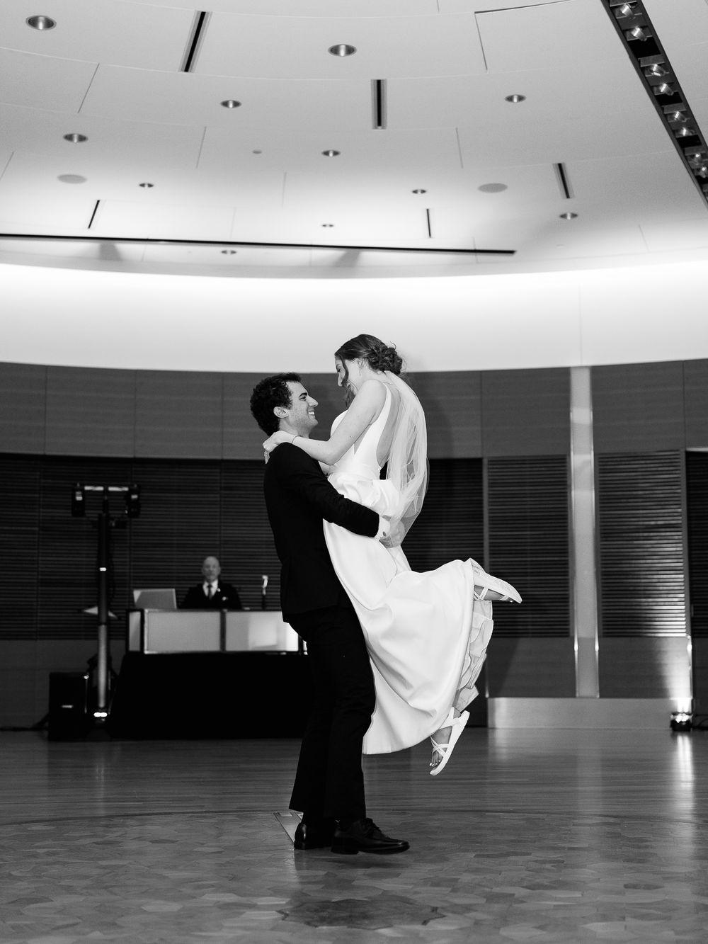 A romantic black and white wedding dance shows a couple embracing as the bride is lifted off the ground in a ballroom setting.