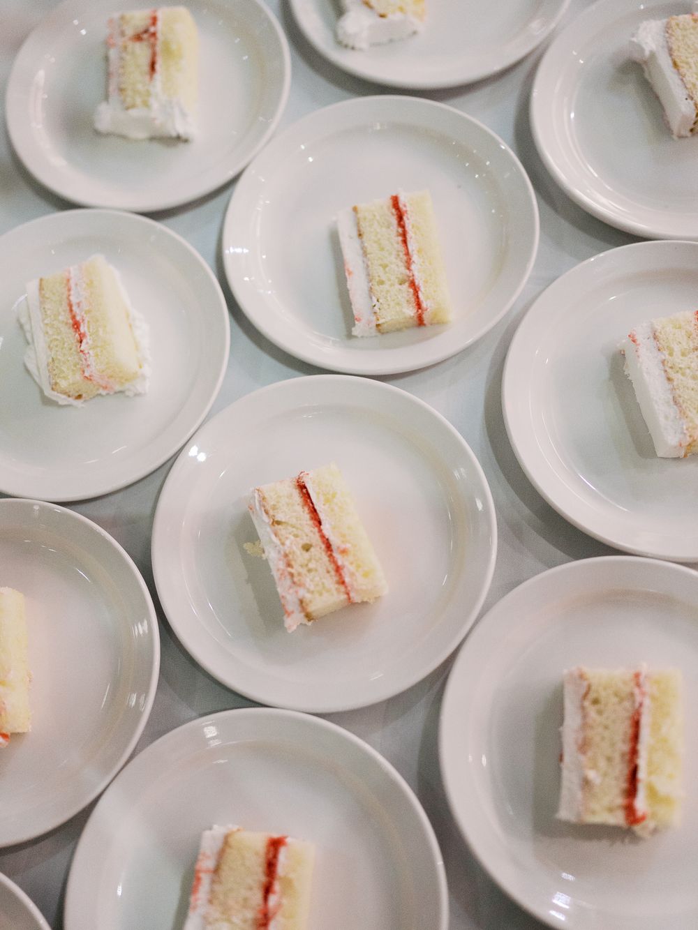 Small slices of layered white cake with red filling arranged on multiple round white plates viewed from above.