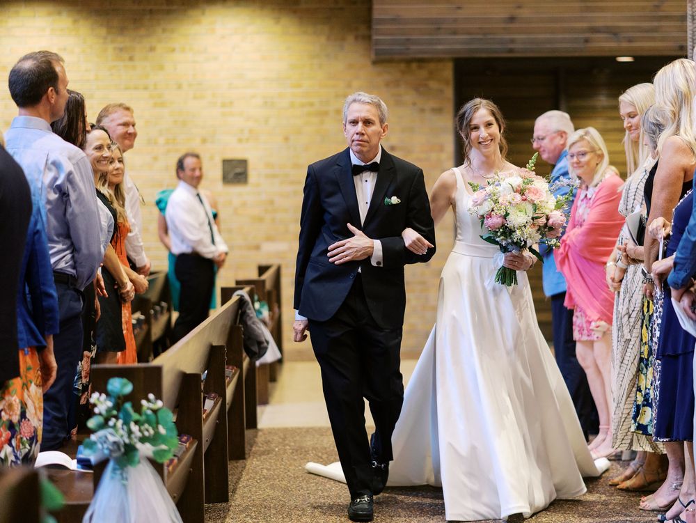 A bride in a white dress and bouquet walks down the church aisle during a traditional wedding ceremony.