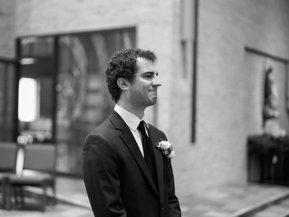 A black and white photo of a groom wearing a dark suit with a white boutonniere looking thoughtfully to the side.