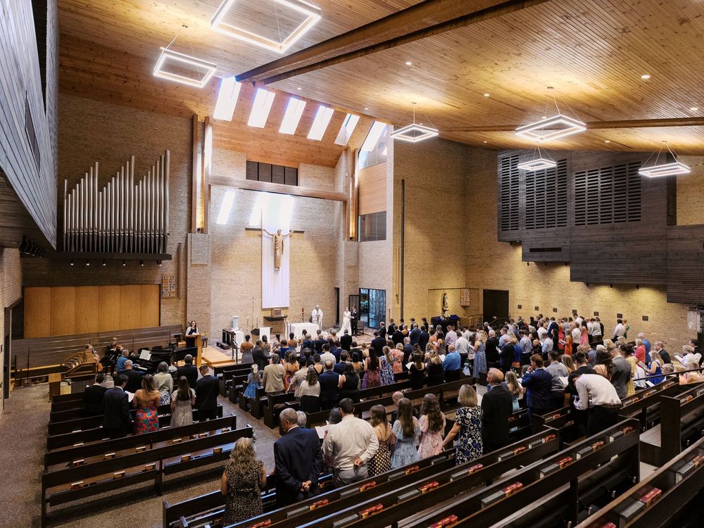 A congregation gathers for service in a modern church sanctuary with wooden walls and organ pipes.