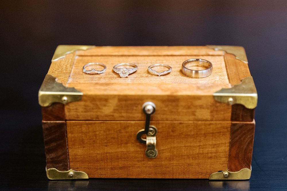 A vintage wooden jewelry box with brass corners and carved decorative details sits against a dark background.
