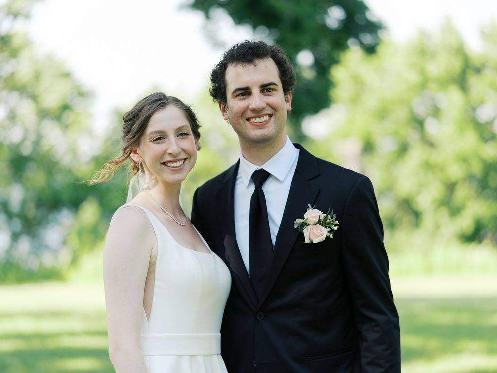 A bride and groom pose outdoors for their wedding portrait in a garden setting with green foliage in the background.