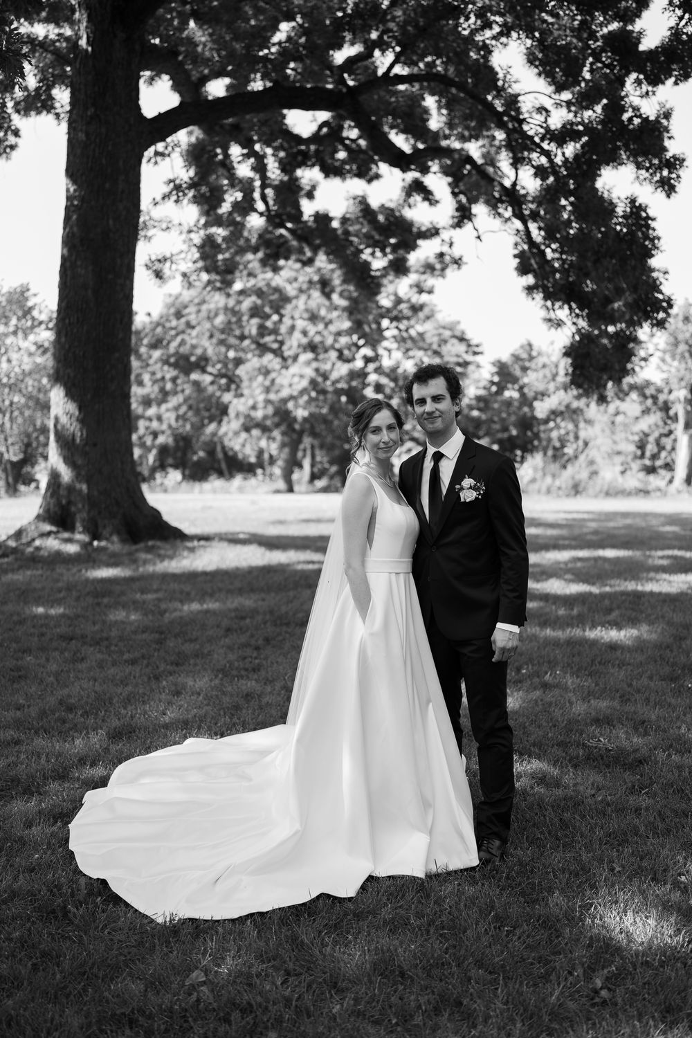 Elegant black and white wedding portraits showing a bride in flowing white dress and groom in dark suit on grassy lawn.