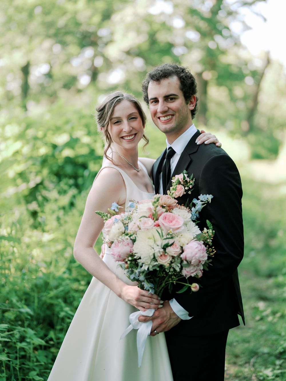A romantic wedding portrait in a lush garden setting with a beautiful bouquet of pink and white flowers.