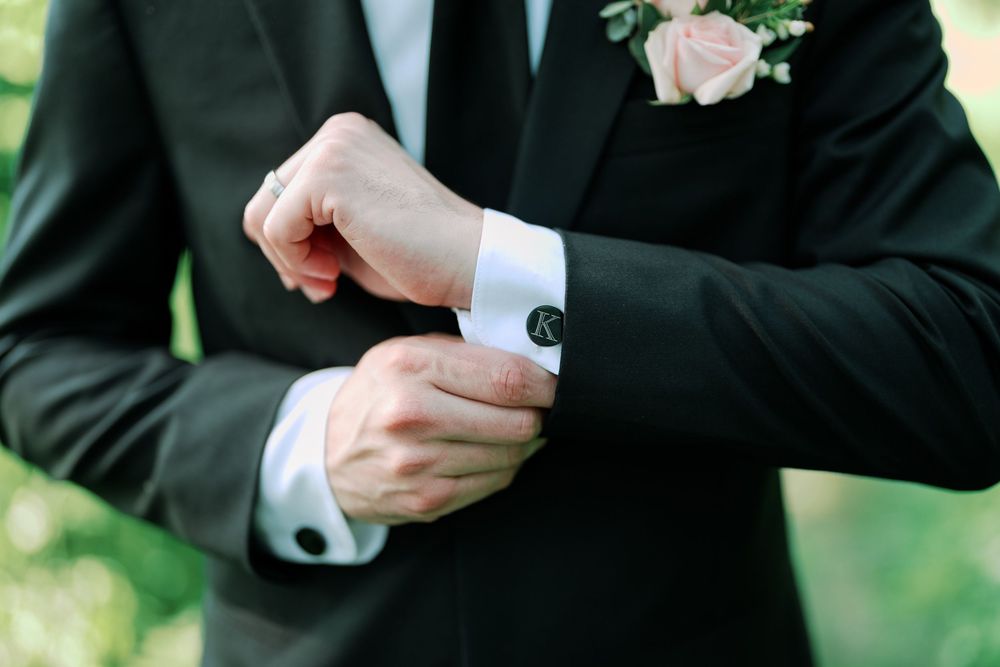 Close-up shot of hands adjusting a bow tie and suit at formal event with blurred green background.