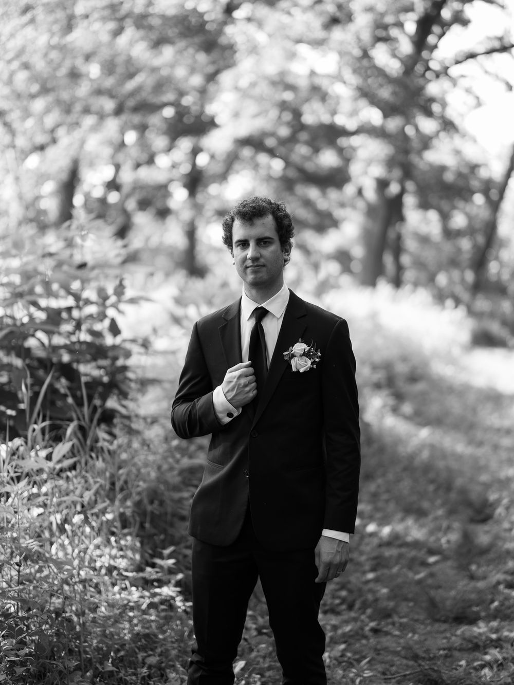 Five black and white portrait photographs show a person in formal attire standing outdoors with a boutonniere.