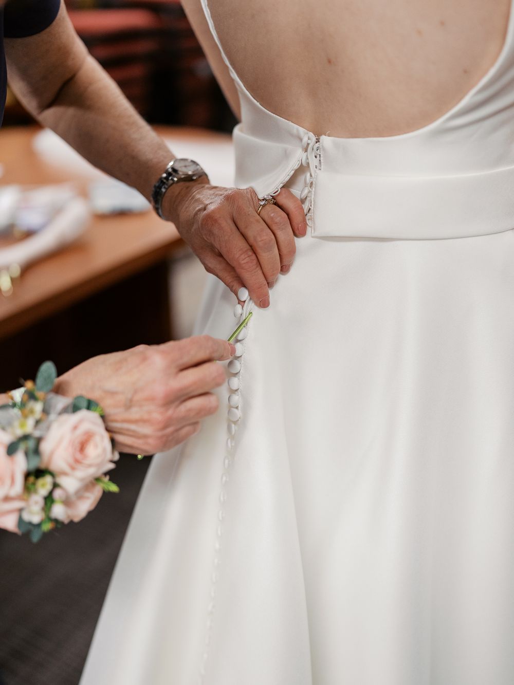 Row of wedding dress detail shots showing someone fastening buttons on elegant white bridal gown.