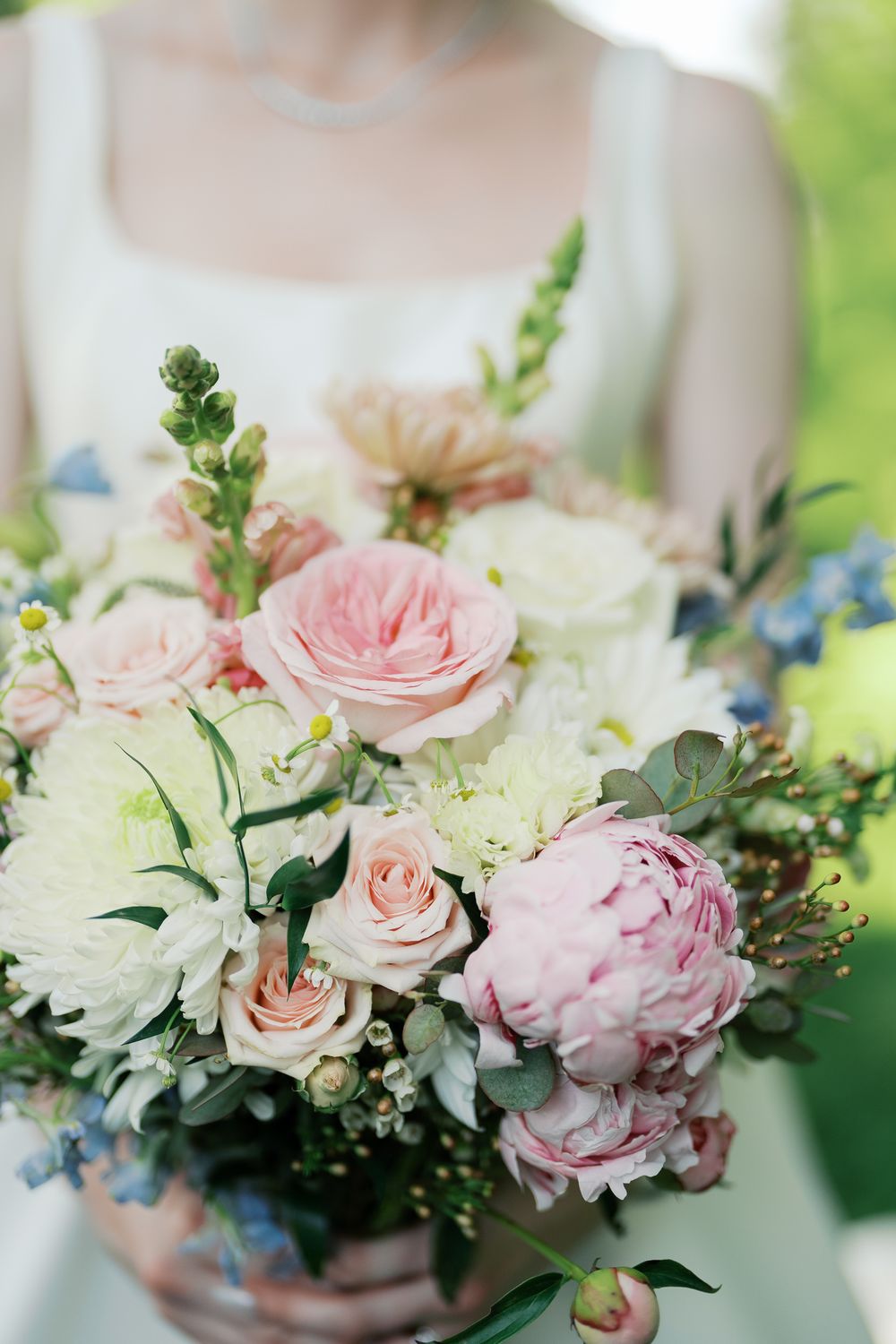 A romantic bridal bouquet featuring pink roses, white peonies, and delicate blue flowers with eucalyptus greenery.