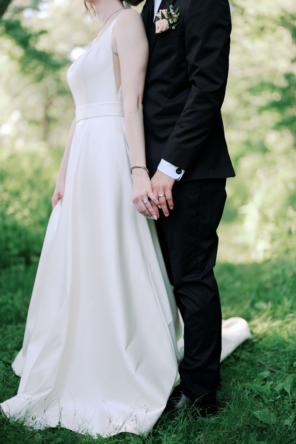 Bride and groom stand together on grassy hill showcasing elegant white wedding dress and classic black tuxedo.