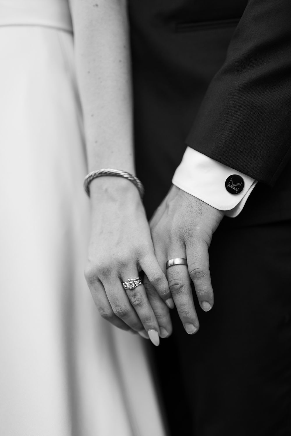 Two hands with wedding rings touch intimately in a black and white photograph.