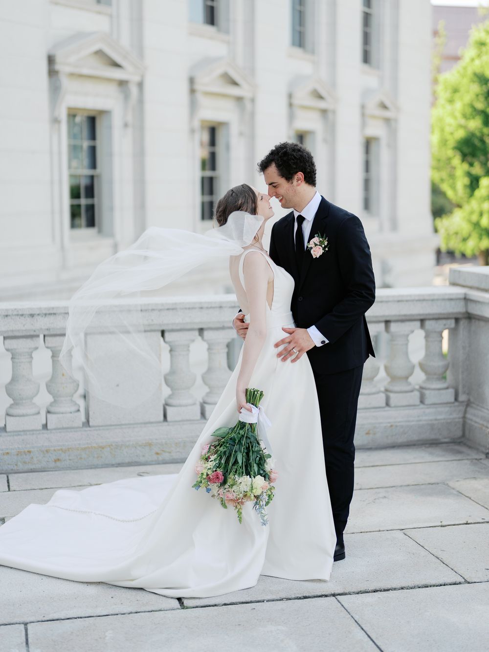 A bride and groom share romantic moments in four candid photos along a white stone balcony.