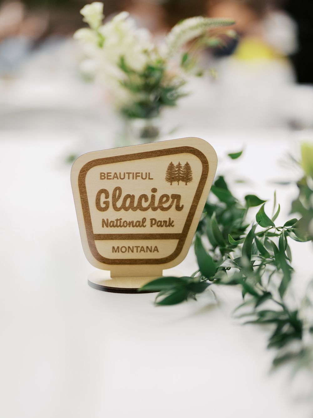 Small wooden national park sign decorations arranged among green foliage on a white tablecloth.