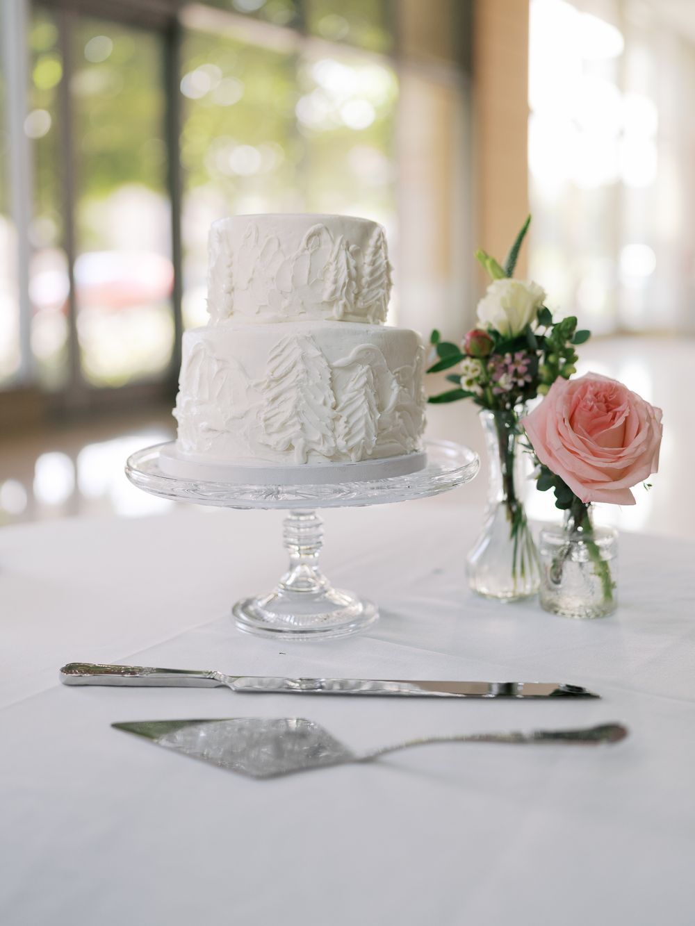 A series of elegant white wedding cakes displayed on glass pedestals with delicate pink rose accents and silverware.
