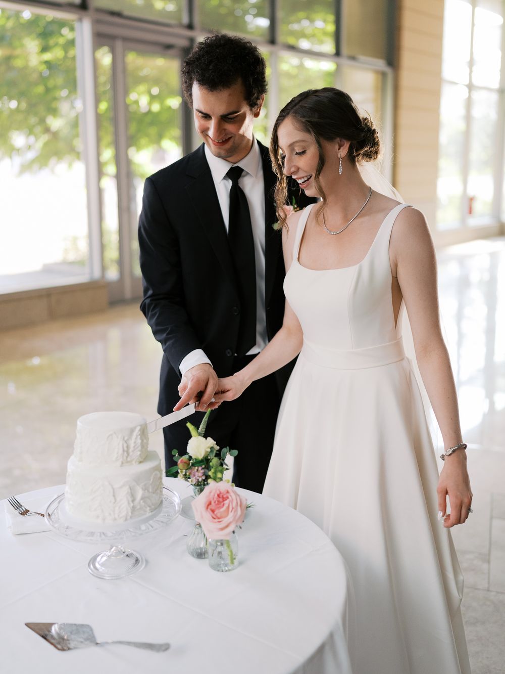 A newly married couple cutting their elegant white wedding cake together at their reception.