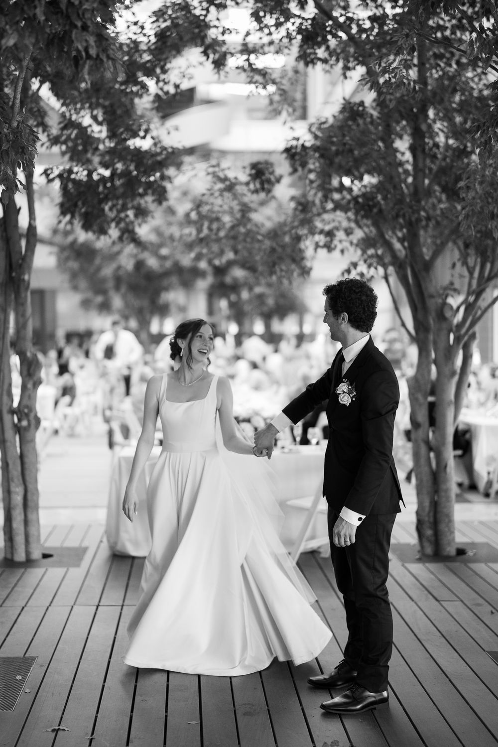 A black and white wedding photo of a couple dancing on a wooden deck surrounded by trees.
