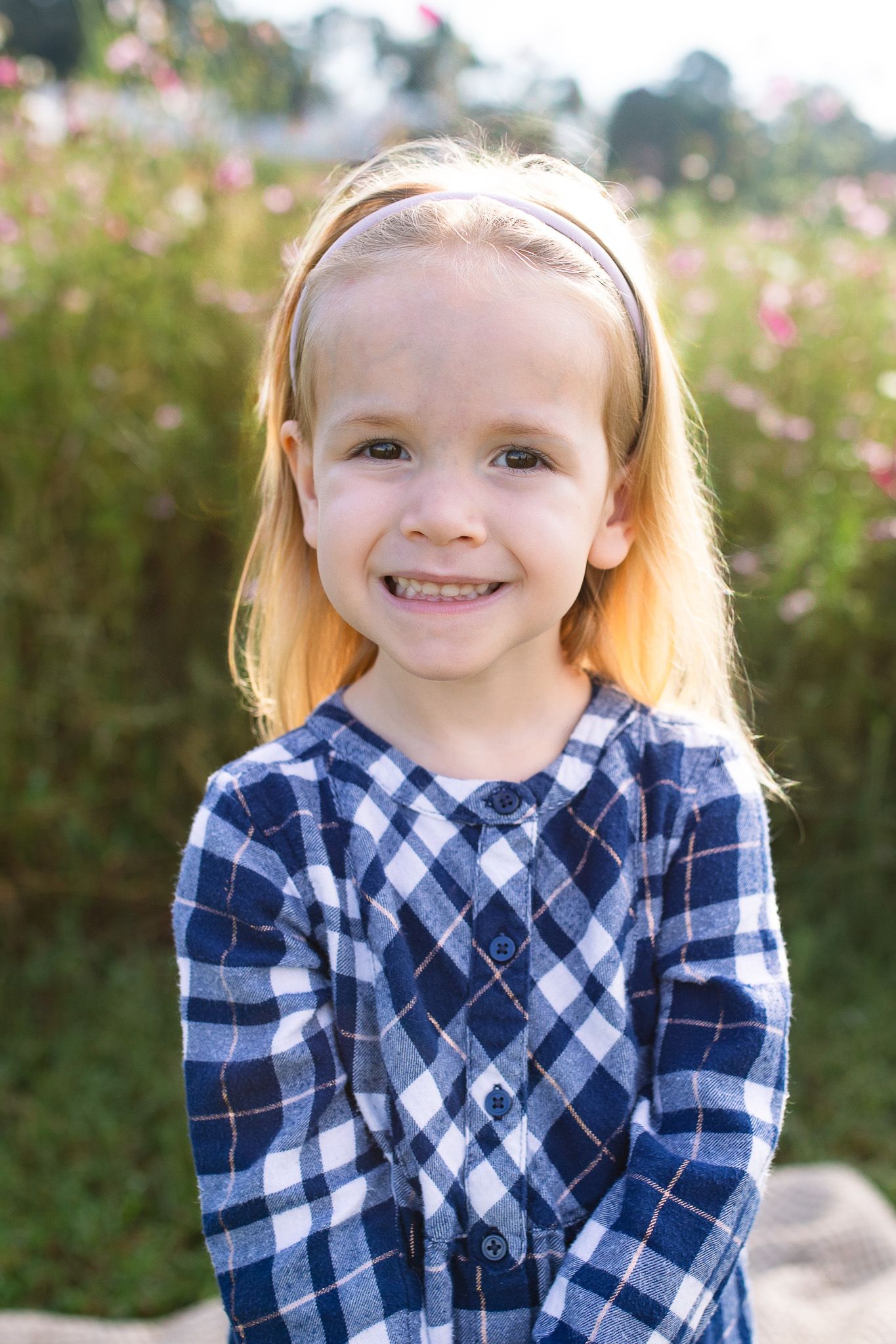 Child wearing navy and white plaid shirt smiles brightly outdoors at Juniper Creek Farm