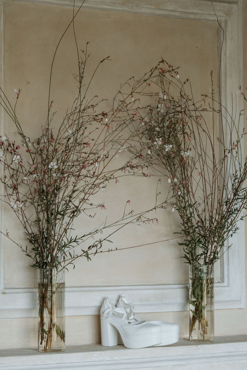 Minimalist decor featuring tall vases of dried branches flanking a white ceramic sculpture against a neutral wall.