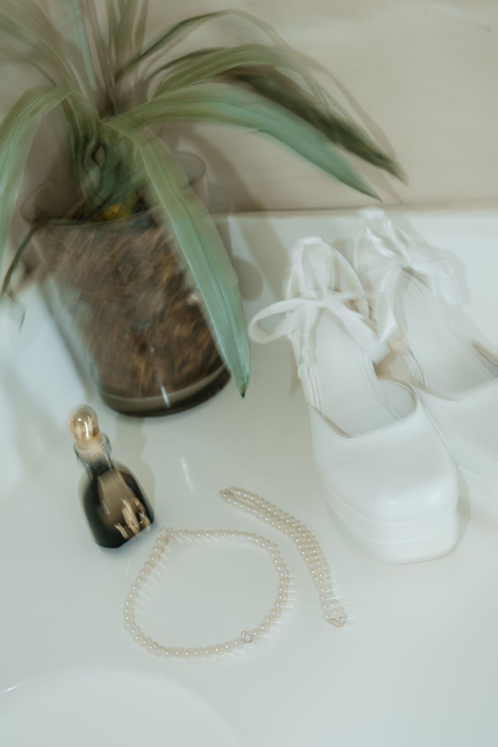 Glass vase with a green air plant and pearl necklace in soft, minimalist white setting.