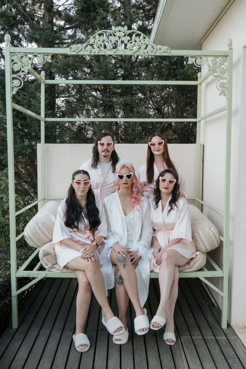 Group in matching white outfits sit on white benches outdoors for a casual photo session in cool sunglasses.