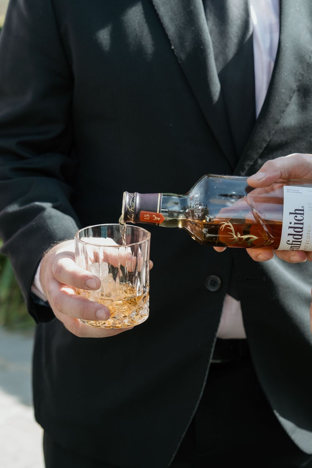Person in black suit pouring golden whiskey into a crystal glass during an elegant occasion.