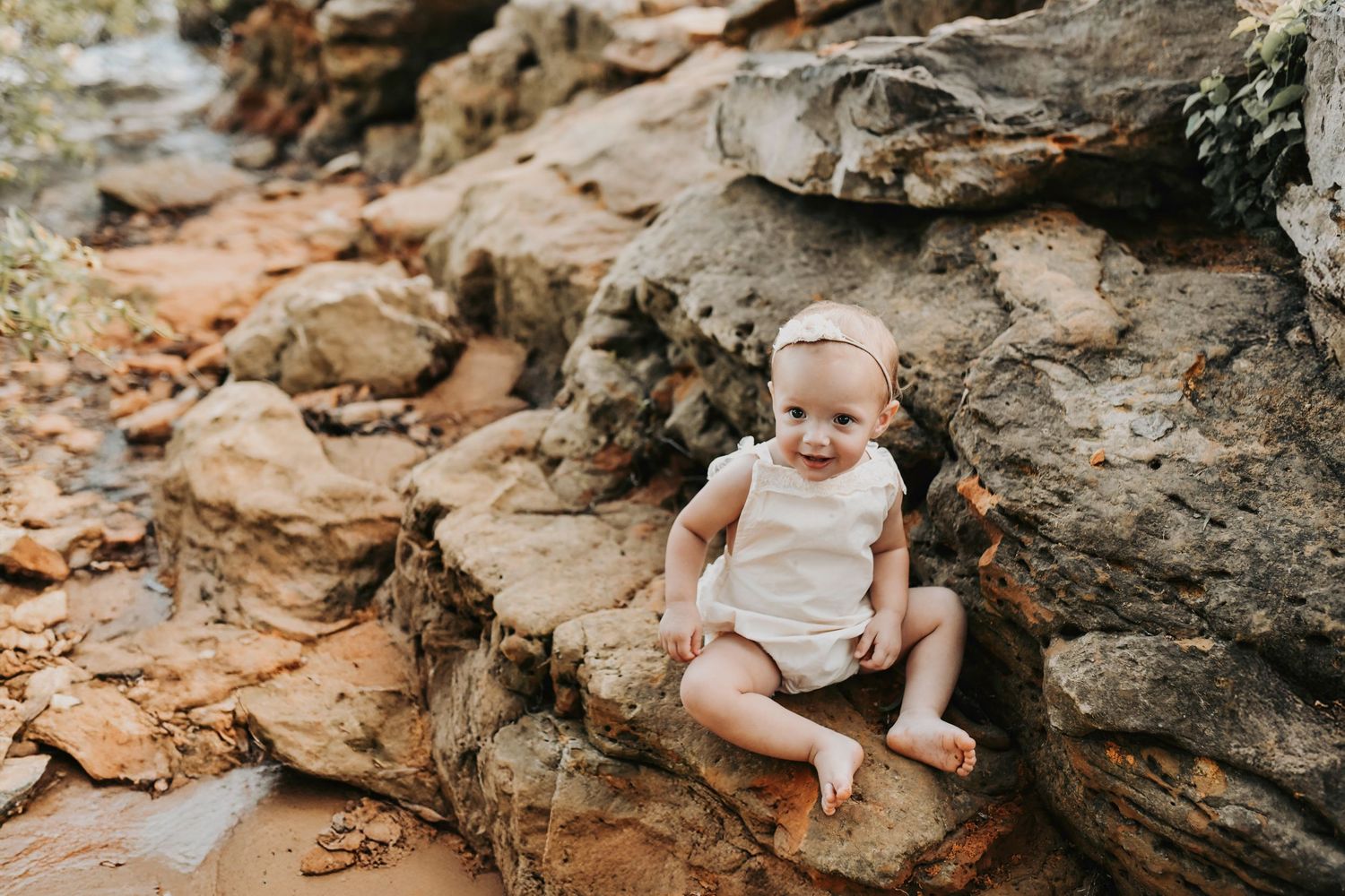 a little girls in a linen lace boho romper sits on rocks on the lake in grapevine