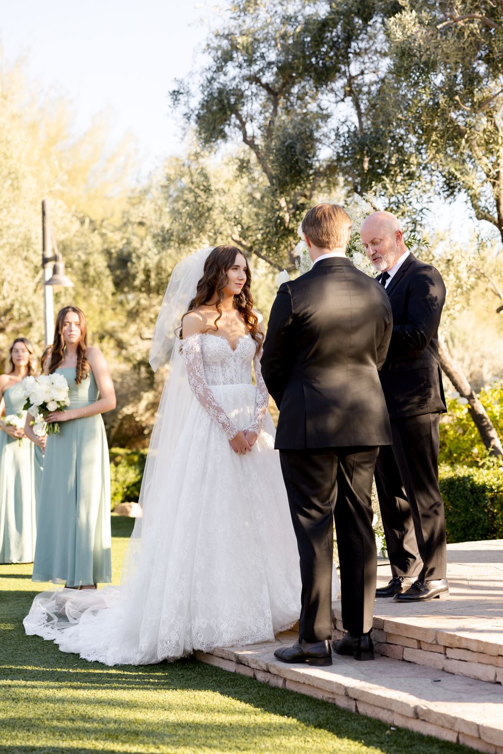 Wedding ceremony taking place outdoors with elegant decorations and floral arrangements on a raised stone platform.