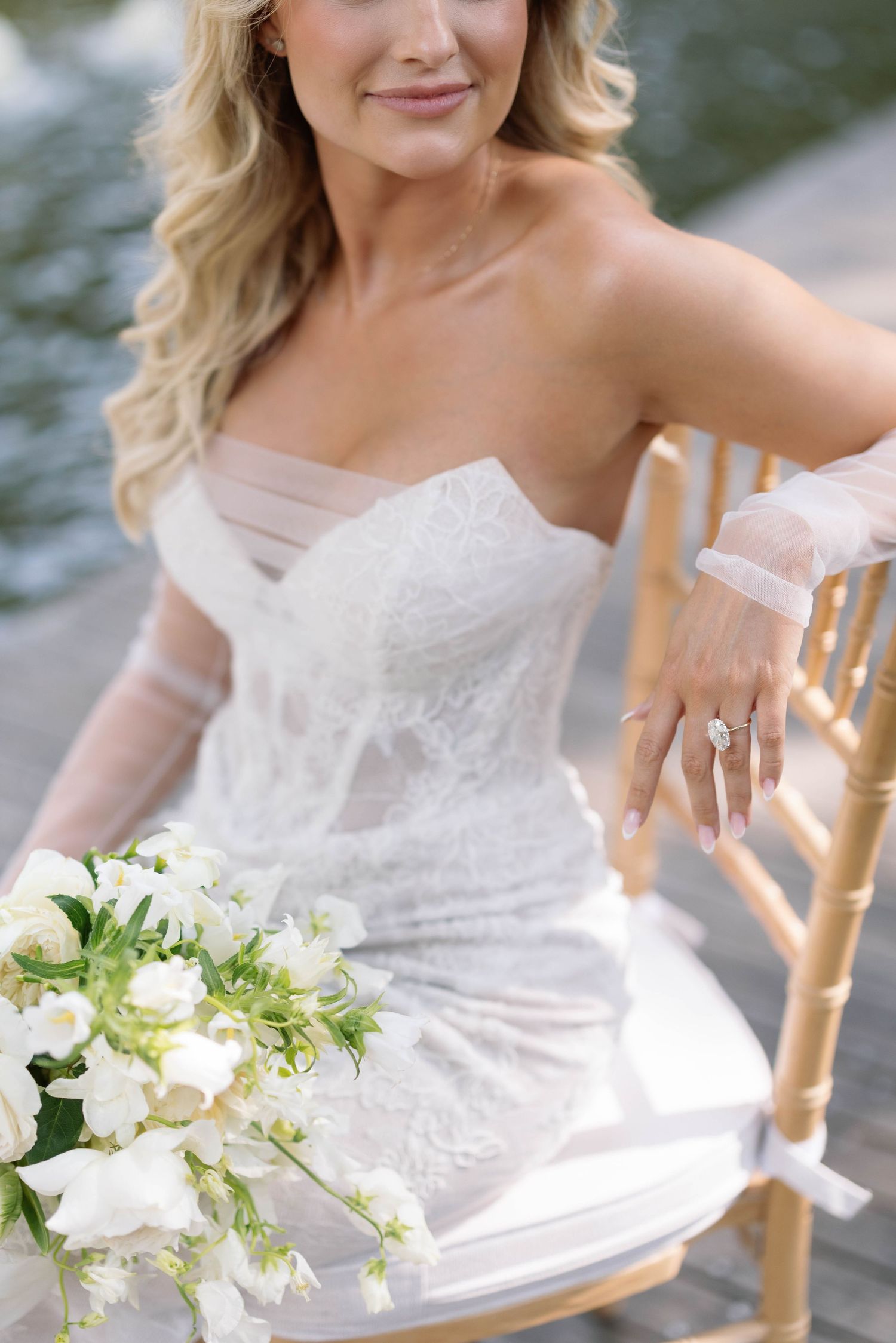 Classic white strapless lace wedding dress shown with elegant ivory bouquet and bamboo chair detail.