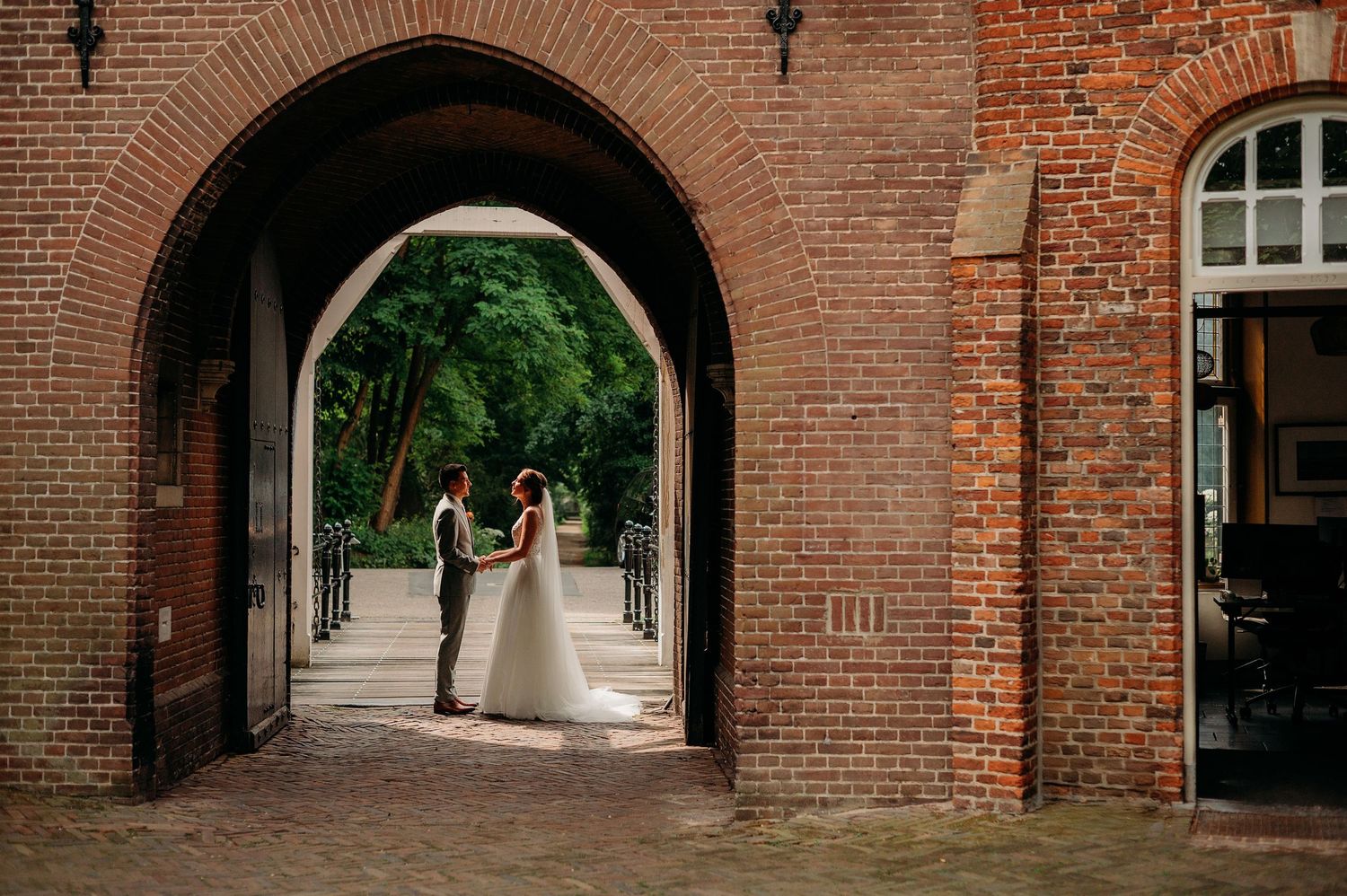 Bride and groom stand silhouetted under a rustic brick archway in an elegant outdoor wedding setting.