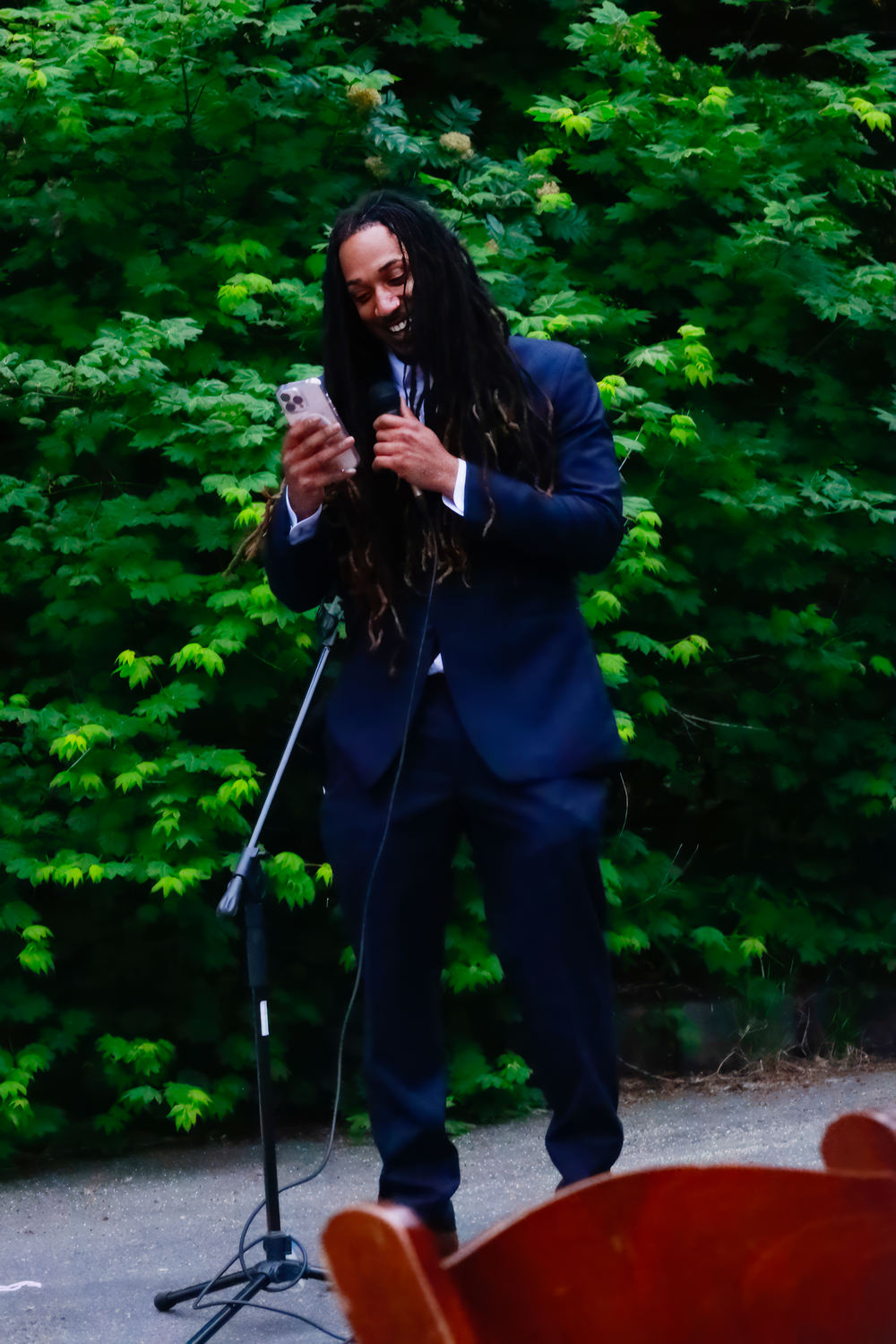 Person in navy blue attire performs on a wooden platform surrounded by lush green foliage.