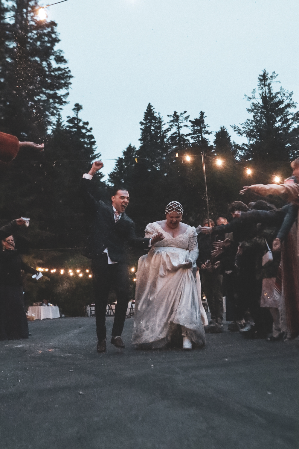 Guests celebrate at an outdoor evening wedding reception with string lights illuminating the dance area.