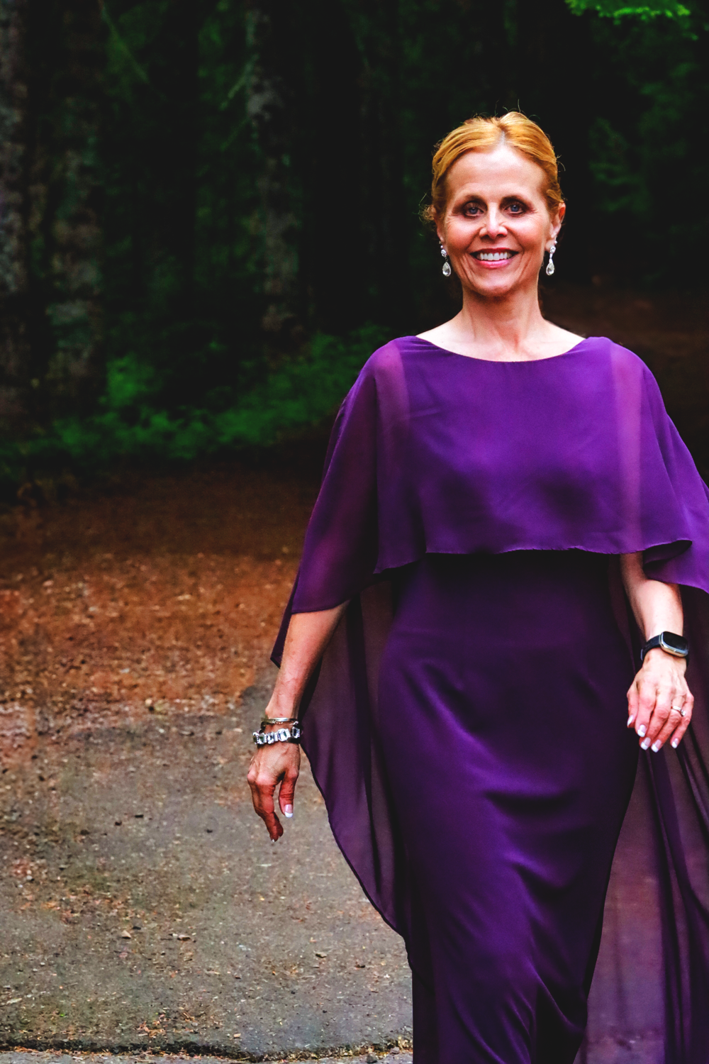 Woman in flowing purple dress poses on a forest path during an outdoor photo session.