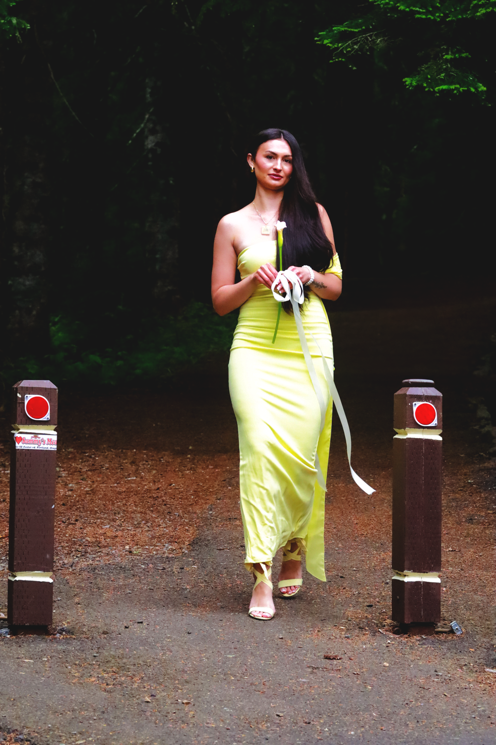 Person in yellow formal dress walks between two posts on forest path.