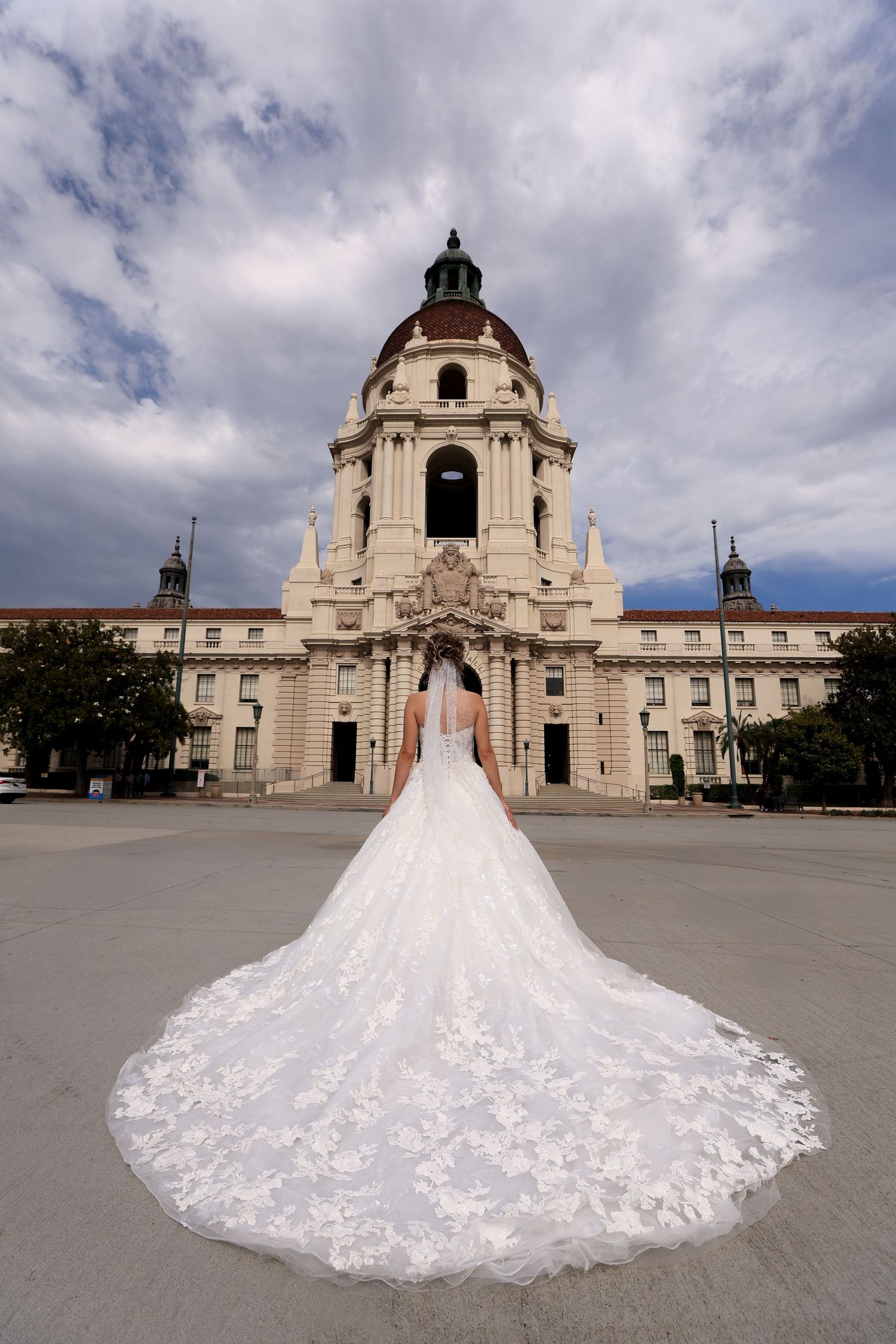 A stunning white wedding gown with long lace train photographed in front of Pasadena City Hall's elegant architecture.