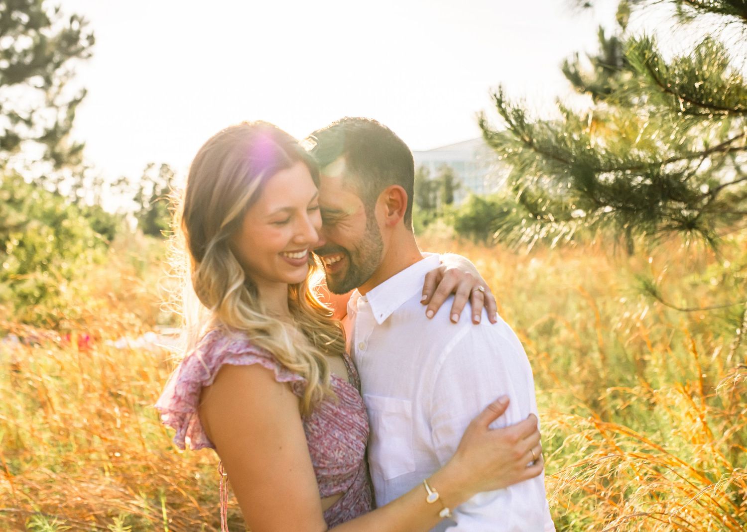Couple embracing in golden sunlit field during sunset as they share an intimate moment together.