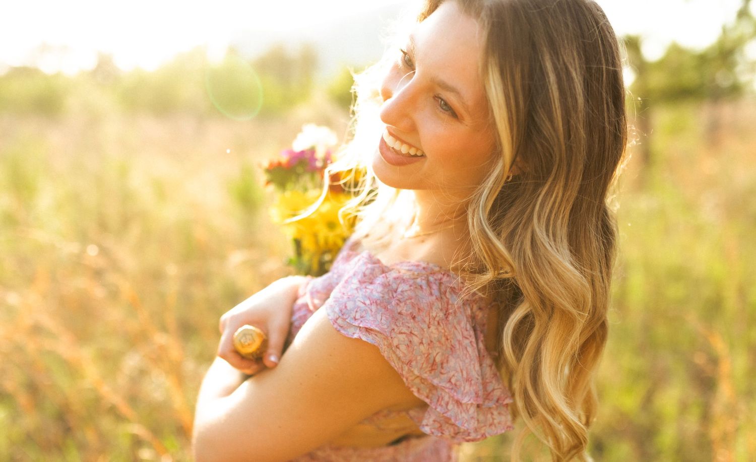 Person in pink dress laughs joyfully during golden hour outdoor photo session on sunny summer day.