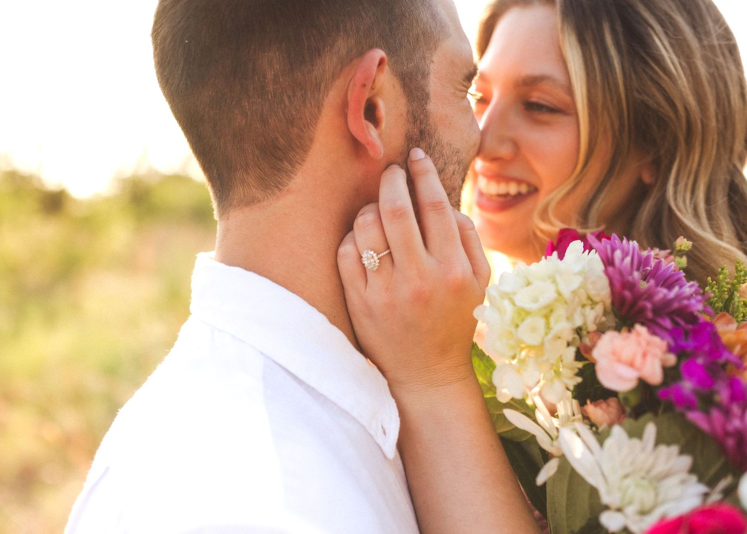 Intimate couple embracing with bride holding vibrant bouquet during golden sunset wedding photo session.