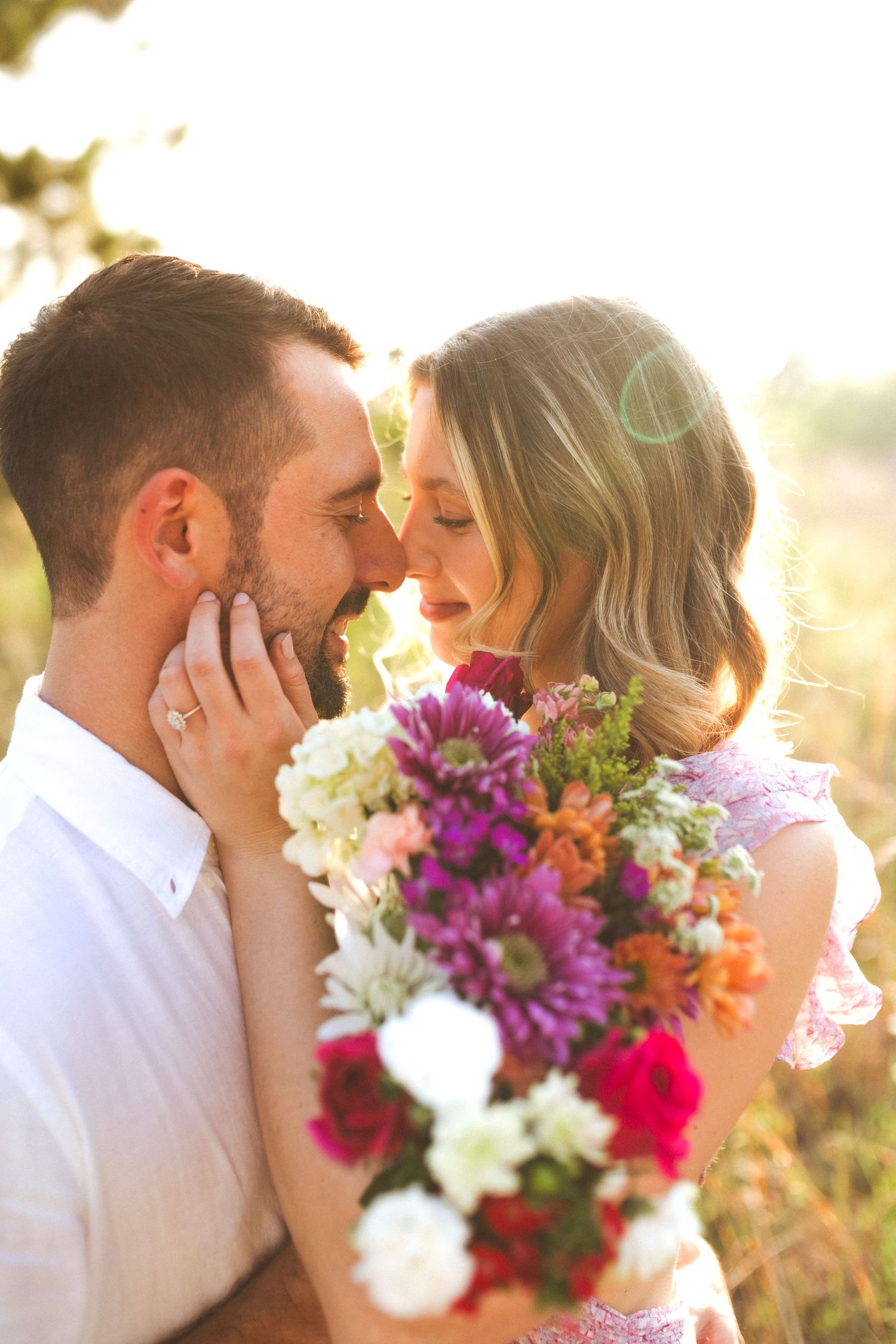 Romantic couple embraces in golden sunlight with vibrant purple and white wedding bouquet during intimate outdoor moment.