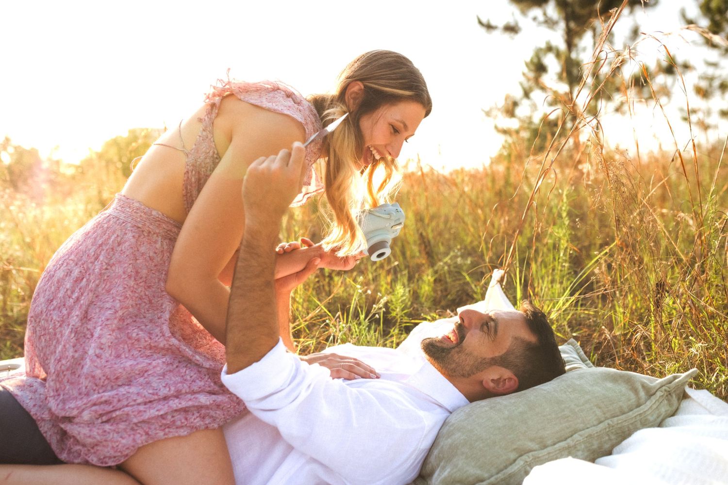 A couple in a field shares an intimate moment at sunset while lying in tall grass.