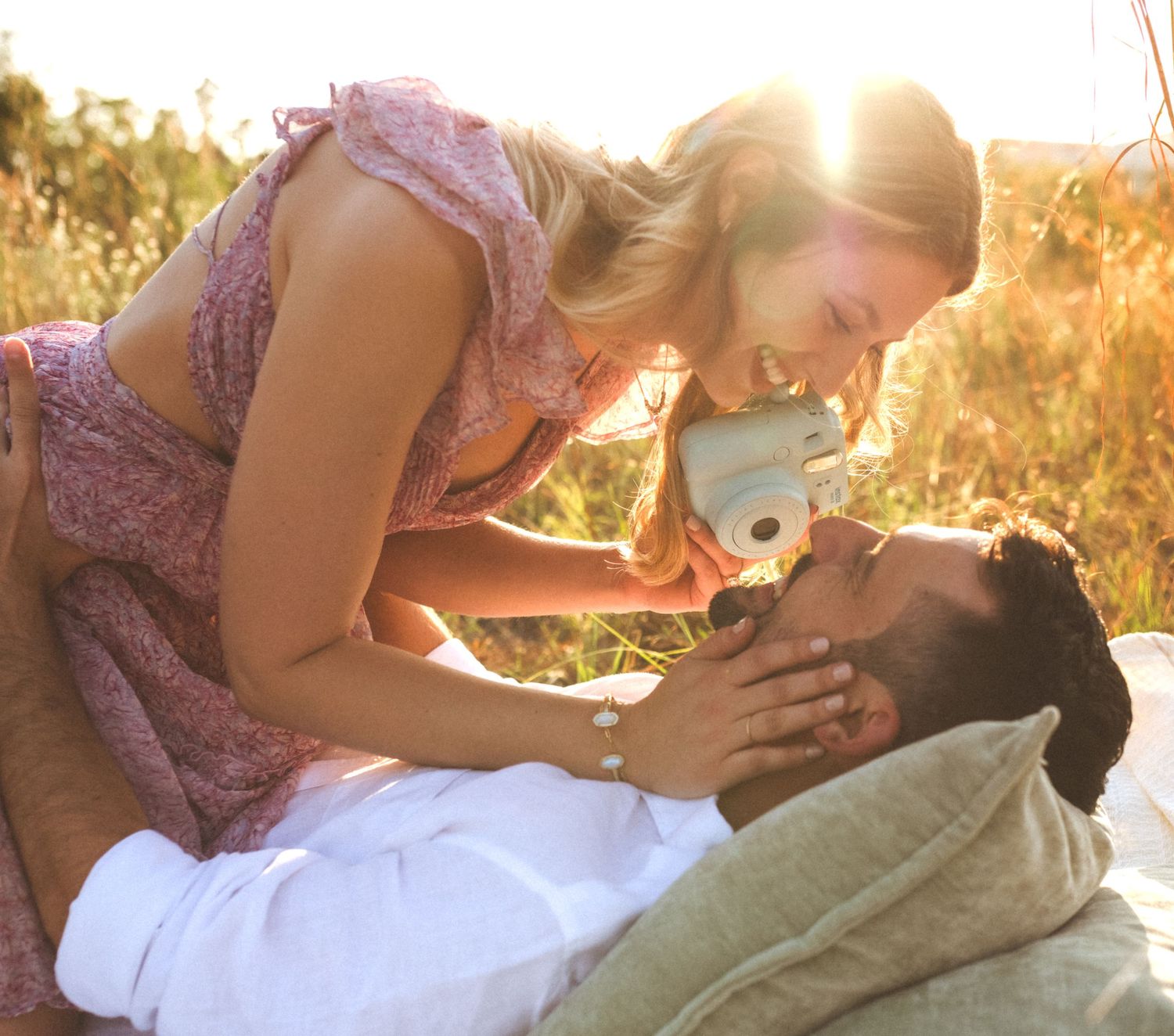 Two romantic figures share an intimate moment in a sunlit golden meadow during sunset, lying in the grass together.