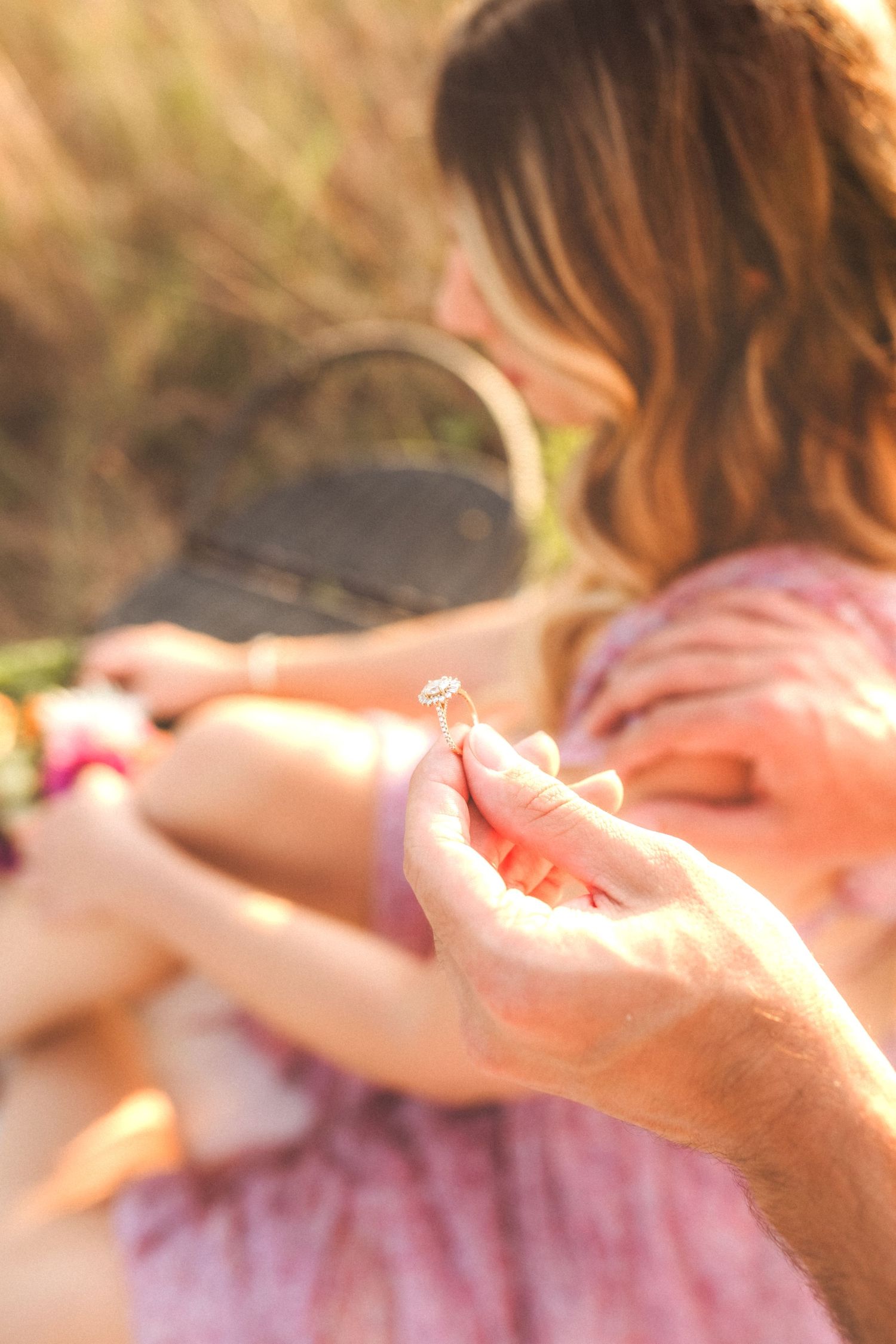 A delicate crystal dandelion seed is held in golden sunlight while wearing a pink dress during a warm summer afternoon.