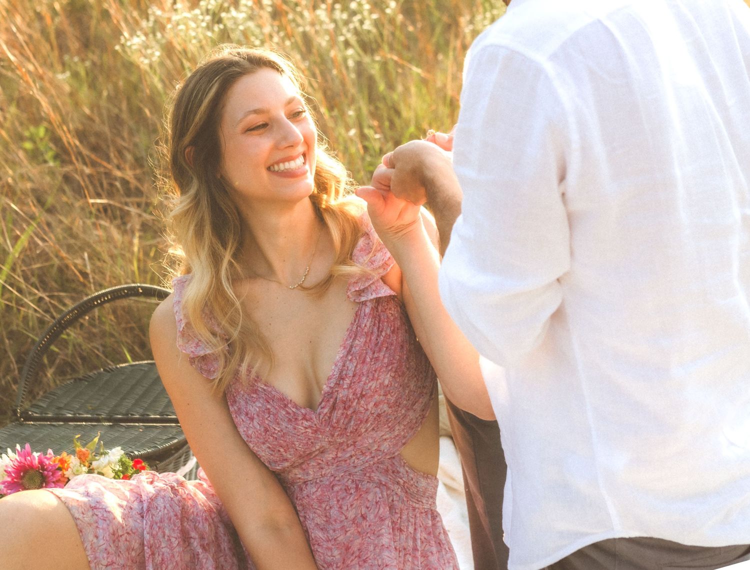 A woman in a mauve floral dress sits outdoors during a romantic photoshoot at golden hour.