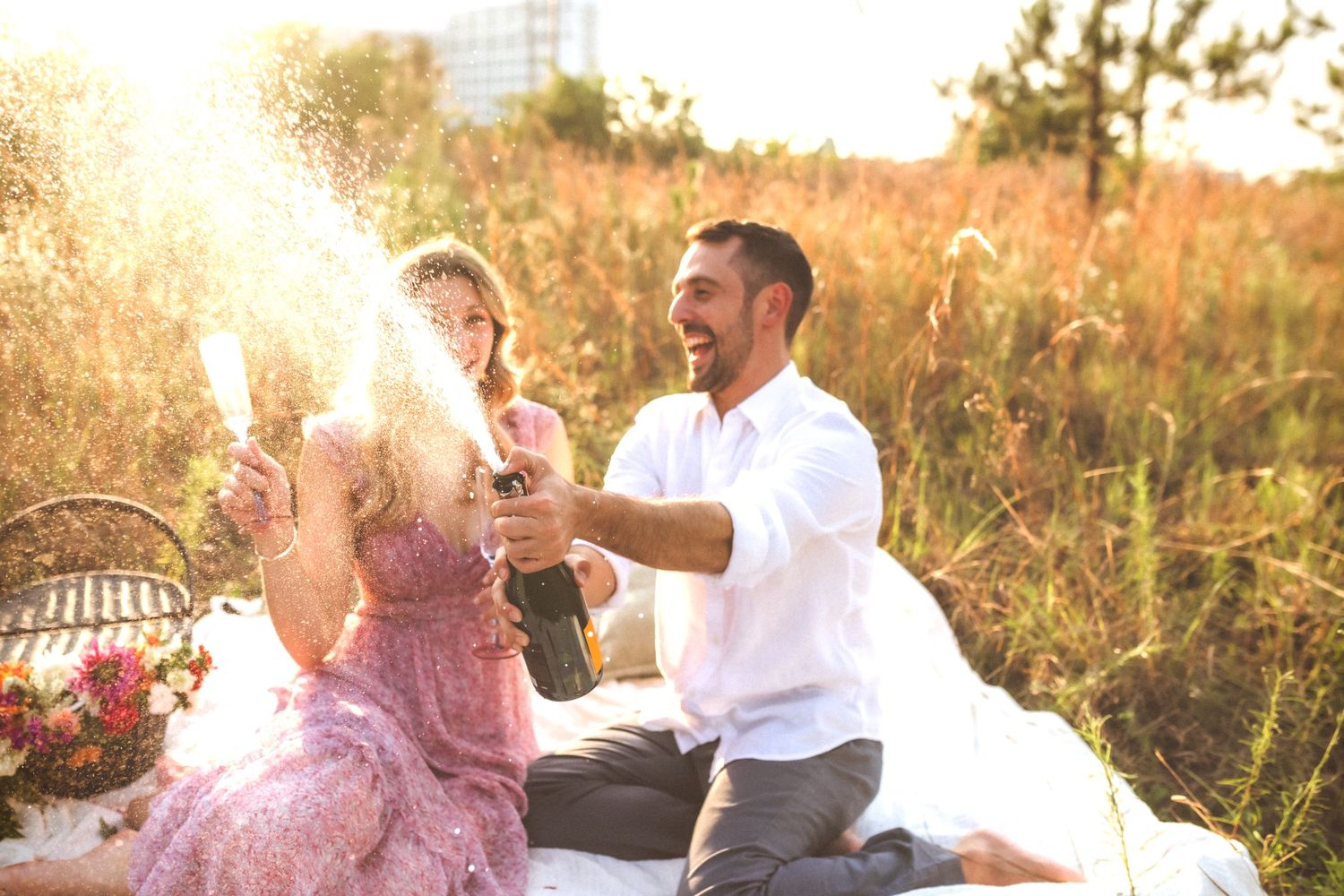 A couple enjoys champagne at a romantic sunset picnic in a golden meadow.