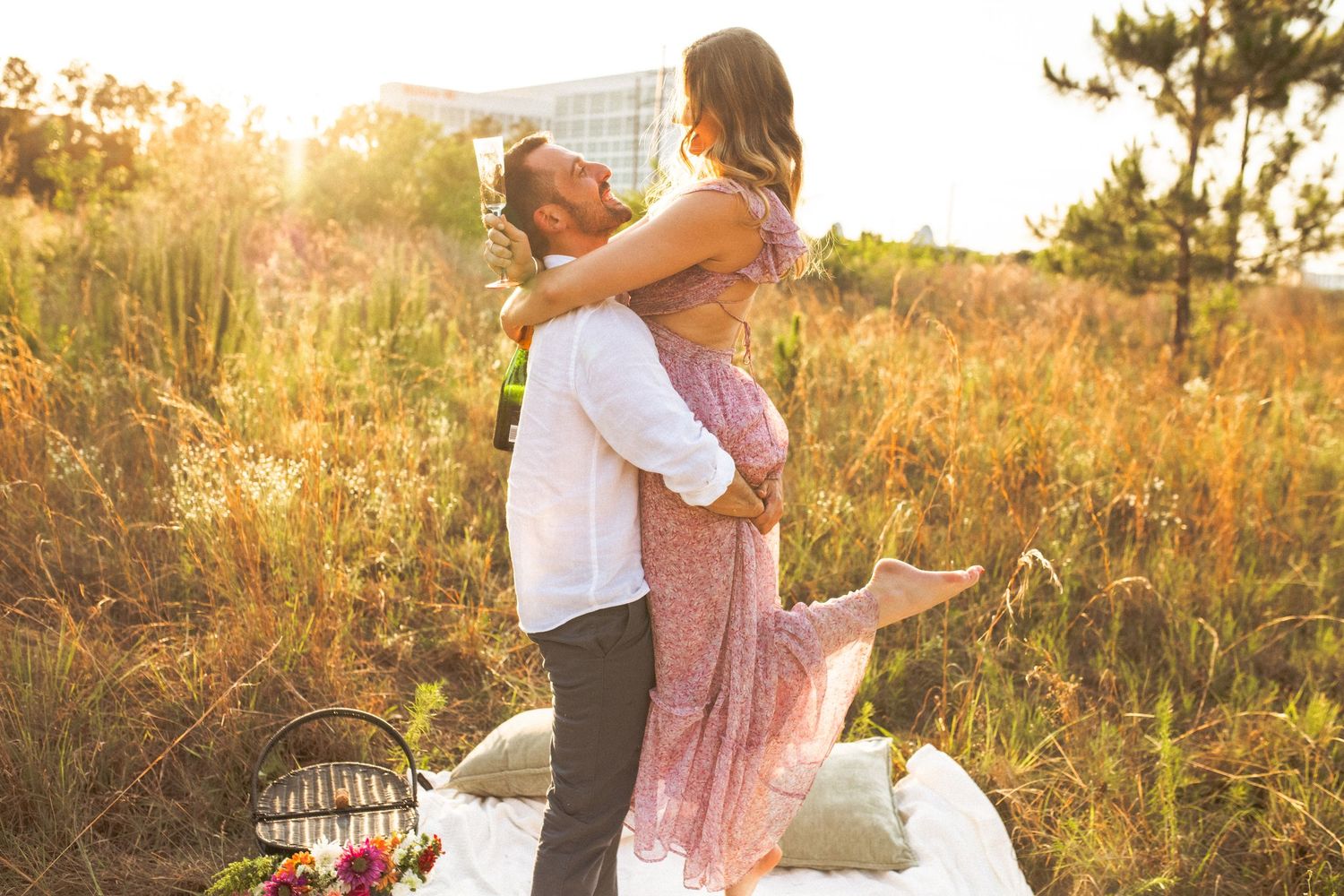 A couple shares a romantic moment in a sunlit meadow during golden hour with a picnic basket nearby.