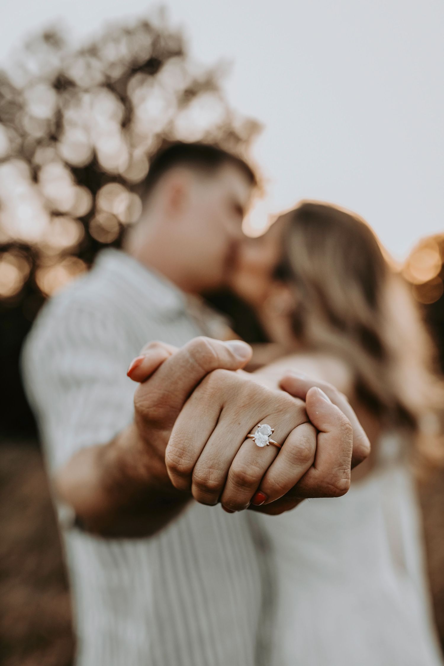 Close-up of couple’s hands intertwined in a dreamy golden field at dusk