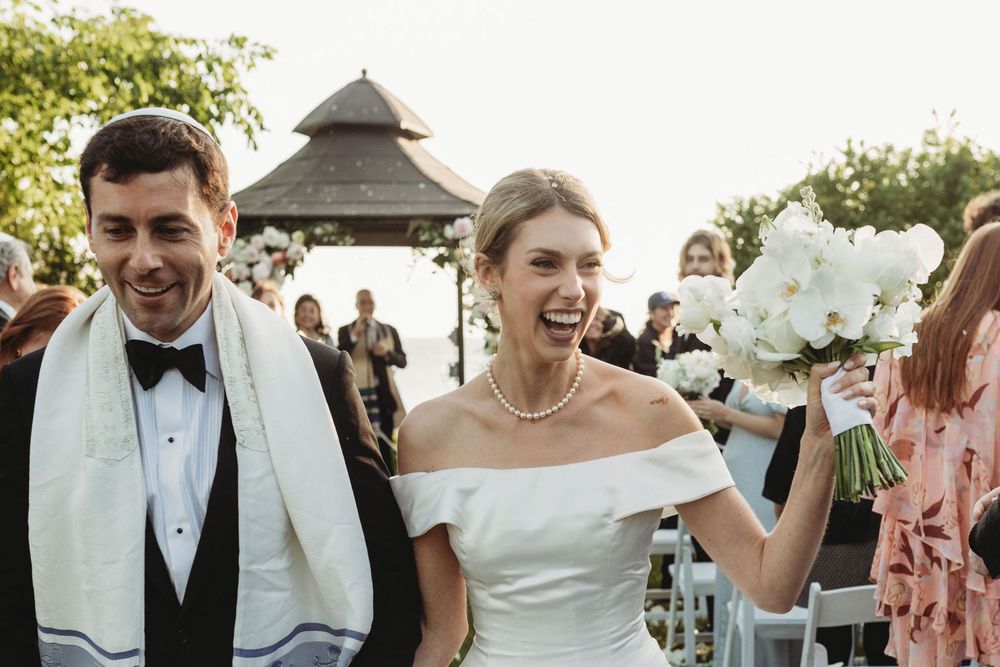 A joyful moment captured at an outdoor wedding ceremony with white florals and an elegant gazebo in the background.