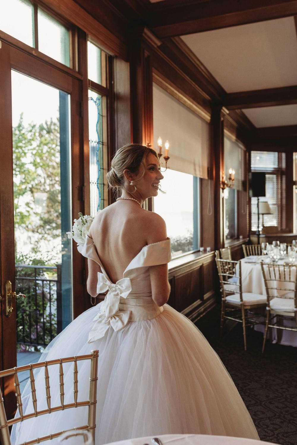 An elegant wedding dress with off-shoulder details and a dramatic tulle ball gown skirt is showcased in a rustic venue.